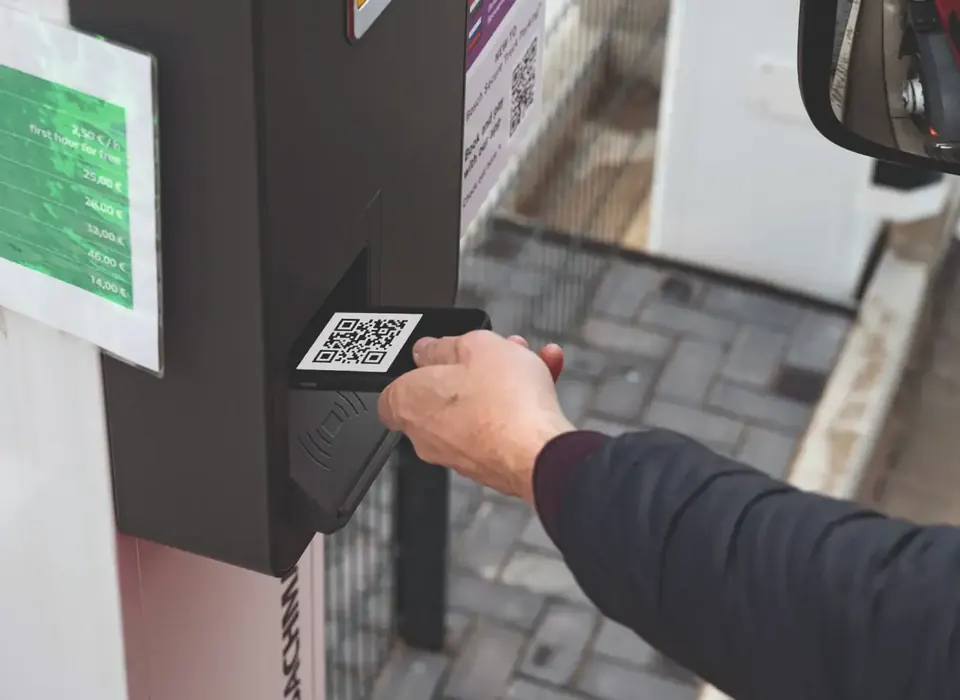 Fahrer hält sein Handy mit QR-Code an das Lesegerät an der Einfahrt